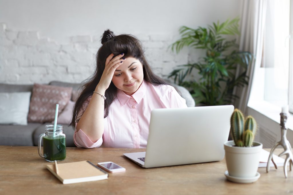People, job, modern electronic gadgets and technologies. Frustrated young overweight brunette woman freelancer feeling tired and stressed while working remotely using laptop pc at home office